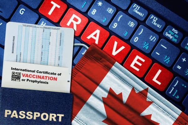 Canada new normal travel concept with passport, boarding pass, face mask with Canadian flag and certificate of COVID-19 vaccination on keyboard. Vaccine passport concept.